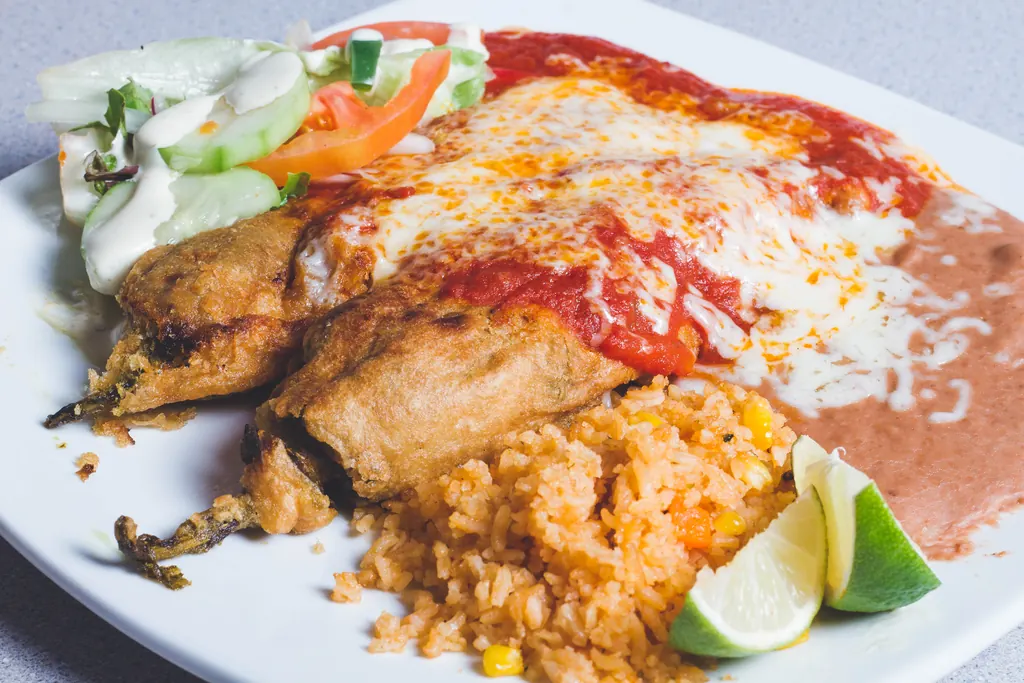 Chiles rellenos bañados en salsa roja y queso derretido, servidos con arroz y ensalada